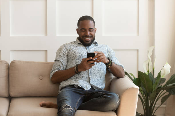 istock African guy sitting on couch chatting online using smartphone 1217477767