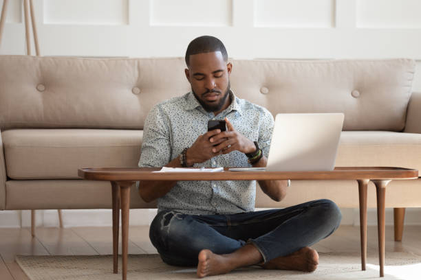 istock African guy sits cross-legged on carpet using smartphone 1217477780