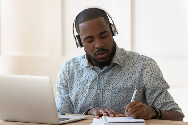 studente africano che indossa le cuffie ascolta il corso audio fa appunti - domestic staff audio foto e immagini stock