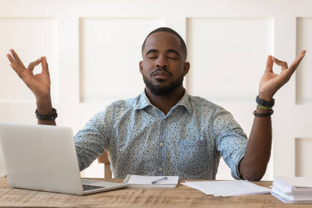 istock African man sitting at desk meditating during workday at workplace 1217477789