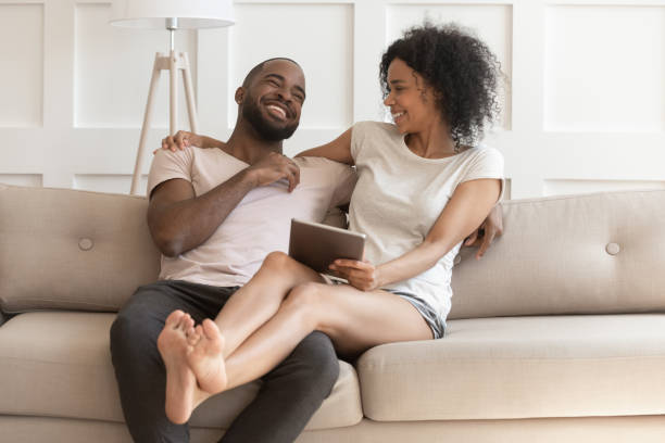 istock African cheerful couple resting on couch with tablet computer 1217477800
