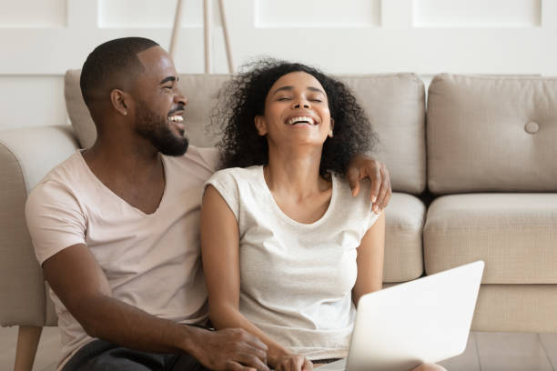 istock Cheerful african couple having fun using online websites at home 1217477808