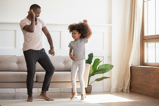 Full length view in cozy warm sunny living room african handsome father dancing with little adorable daughter, family spending time on weekend together, enjoy life listening favourite music concept