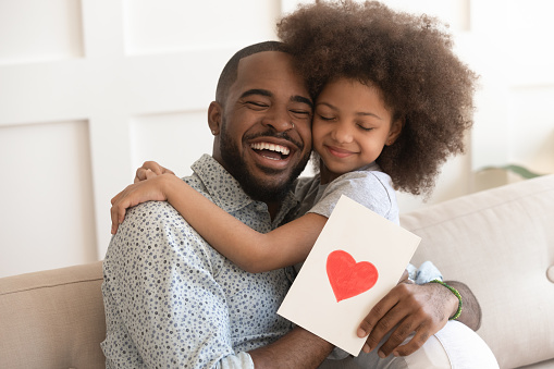 African daddy on Father Day received from caring little daughter paper postcard written message best wishes, drawn red heart as symbol of love and deep affection, family holidays celebration concept