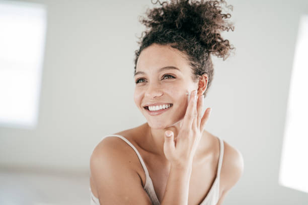 Smiling young women applying moisturiser to her face Smiling young women applying moisturiser to her face distillery still photos stock pictures, royalty-free photos & images
