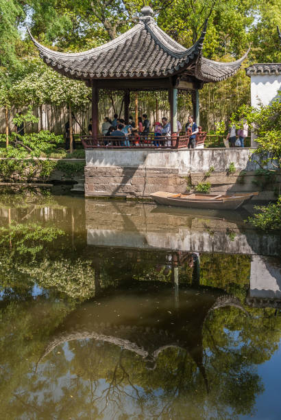 Canal reflects pavilion at Humble Administrators garden, Suzhou, China. Suzhou China - May 3, 2010: Humble Administrators Garden. Pavilion in traditional architecture is reflected greenish water of canal. Green foliage as background. People stand under roof. lake tai stock pictures, royalty-free photos & images