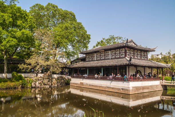 Large building at Humble Administrators garden, Suzhou, China. Suzhou China - May 3, 2010: Humble Administrators Garden. large traditionally built building at pond with bridge set in green environment under blue sky. People present. suzhou creek stock pictures, royalty-free photos & images
