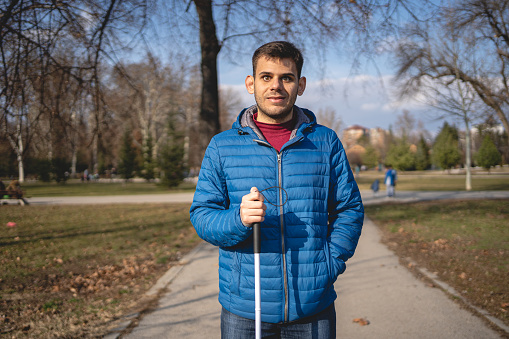 Young man with blindness disability enjoying a warm spring day at a park with a blind persons cane.
