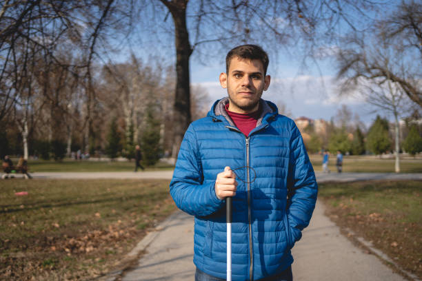 Young man with visual impairment holding a blind persons cane at a park