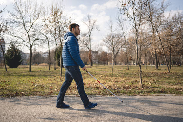 istock Young man with vision problems walking with a blind persons cane at a park 1217483962