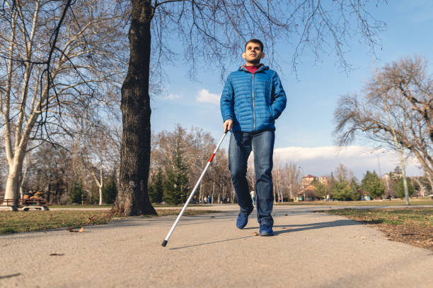 Young man with visual disability walking with a help of a walking cane Young man with blindness disability walking with a blind persons cane outdoors in a park. blind persons cane stock pictures, royalty-free photos & images