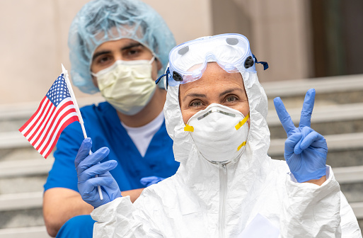 Health care workers during a break looking at the camera holding a US flag showing a two fingers victory sign