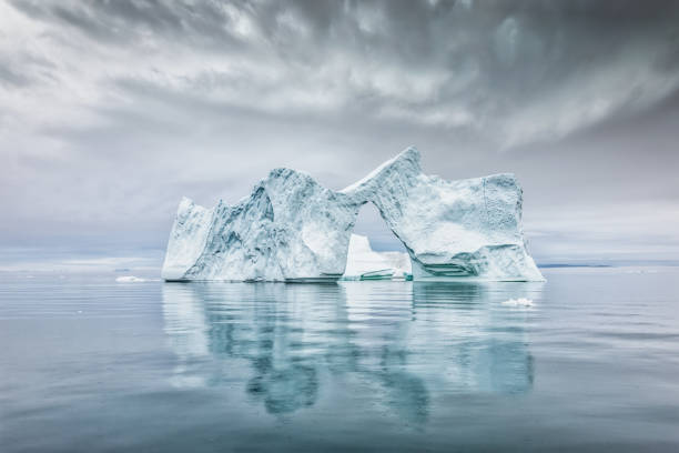 Arctic Ocean Natural Iceberg Arch Greenland Ilulissat Bay Iceberg Ice Arch - Greenland Icebergs Illulissat Bay. Large Iceberg with natural ice arch drifting on tranquil polar waters. Arctic Ocean, Disko Bay, Ilulissat, Greenland, Europe. arctic ocean photos stock pictures, royalty-free photos & images