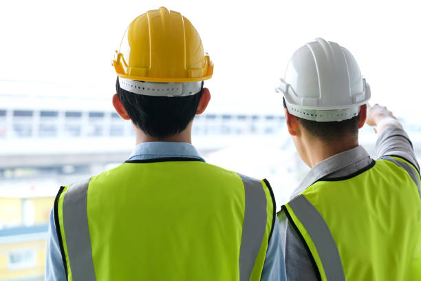 istock Two engineers man standing in front of the site. Right engineer holding paper roll and point to construction area 1217504656