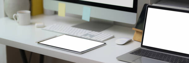 istock Cropped shot of office desk with blank screen laptop, tablet and computer on white table 1217513574
