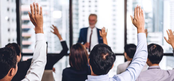 Businessman standing in front of group of people in consulting meeting conference seminar and showing hand to answer question at hall or seminar room.presentation and coaching concept stock photo