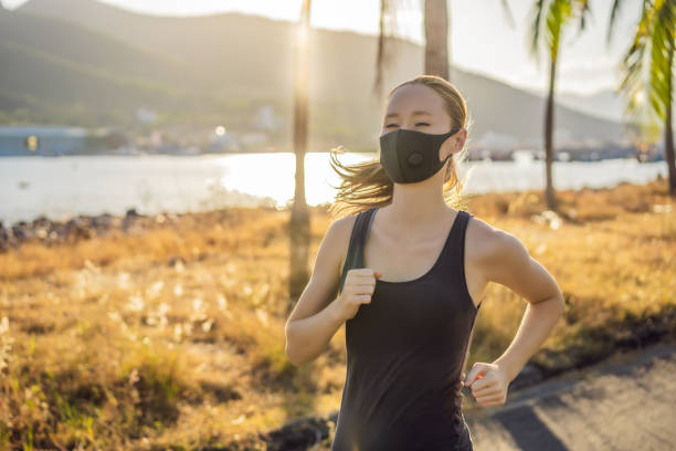 corredor usando máscara médica, pandemia coronavírus covid-19. esporte, vida ativa em quarentena cirurgia esterilizando proteção da máscara facial. corrida ao ar livre na pista de atletismo em corona outbreak. mantenha sua forma durante a quarentena, - passadeira via pública - fotografias e filmes do acervo