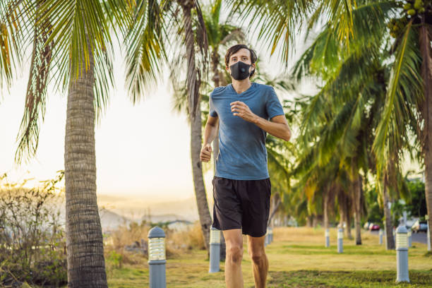 Runner wearing medical mask, Coronavirus pandemic Covid-19. Sport, Active life in quarantine surgical sterilizing face mask protection. Outdoor run on athletics track in Corona Outbreak. Keep your shape during quarantine, pandemic. Runner wearing medical mask, Coronavirus pandemic Covid-19. Sport, Active life in quarantine surgical sterilizing face mask protection. Outdoor run on athletics track in Corona Outbreak. Keep your shape during quarantine, pandemic. Young attractive guy in a black medical mask prepares for a jogging in countryside. human cardiopulmonary system audio stock pictures, royalty-free photos & images