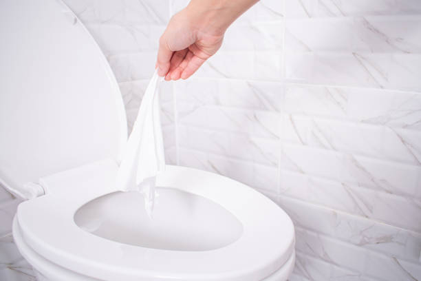 fermez-vous vers le haut de la main jetant le papier hygiénique aux toilettes dans une salle de bains blanche de tuile. - ribbing photos et images de collection