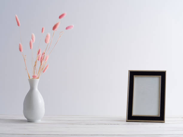 istock Black frame mock up with pink bunny tail grass in vase on white table. Empty frame mockup. 1217526343