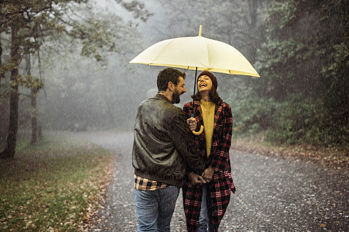 a beautiful smiling young couple of tourists, walking in the rain with a suitcase and a large umbrella