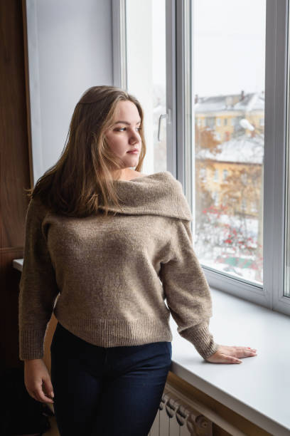 istock Brunette young girl near window. Plus size model 1217529165