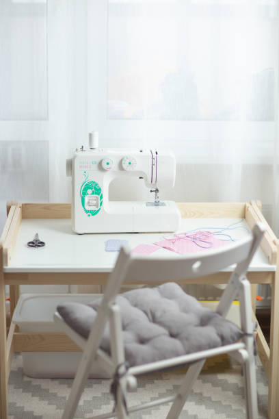 istock How to sew face mask, protective mask sewing process, pieces of dotted cloth, threads and sewing machine on white table with white chair. 1217530217