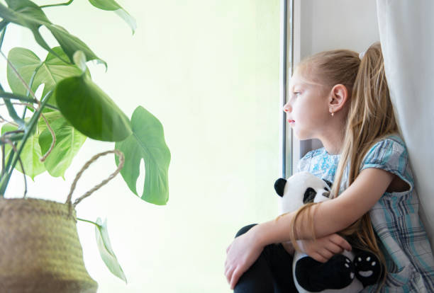istock Sad child girl by the window 1217531311