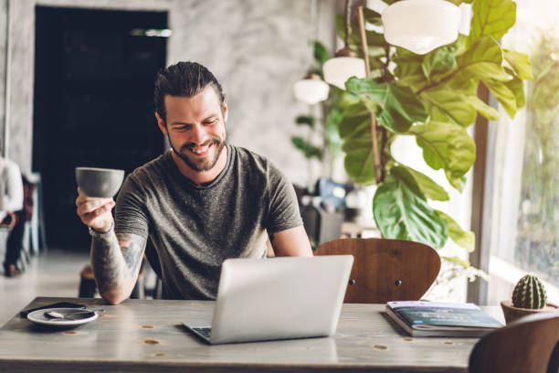 istock Handsome bearded hipster man use and looking at laptop computer with coffee at table in cafe.Communication and technology concept 1217534563