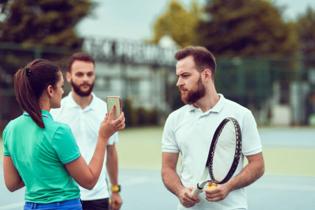 스마트 폰에 남성에게 새로운 테니스 코트 훈련 시간표를 보여주는 여성 - tennis court sports training tennis net 뉴스 사진 이미지