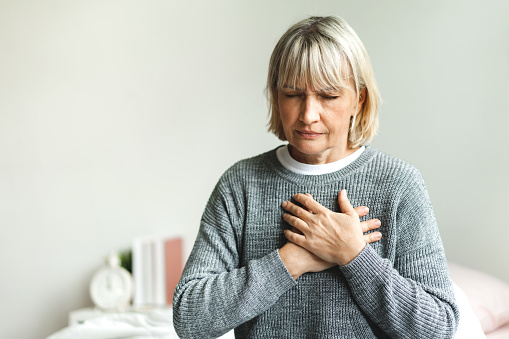 Senior adult elderly women sit on bed with chest pain suffering from heart attack in the bedroom.Healthcare and medical concept