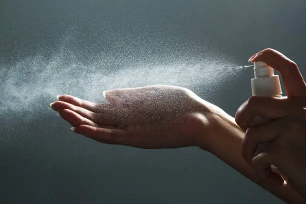 Close-up view of human hand and antiseptic spray bottle on dark background. Sanitation of hands. Control Epidemic Prevention measures of coronavirus.