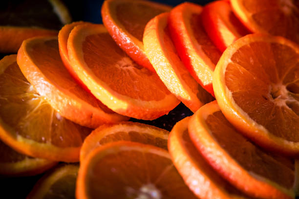 Color image depicting an arrangement of slices of fresh oranges stacked and in a row. Abstract macro compositions with warm back light.