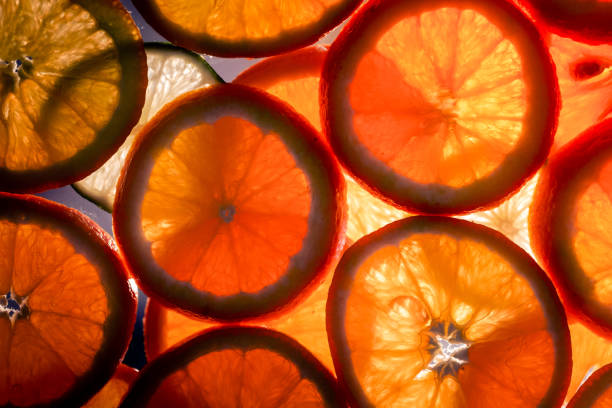 Color image depicting an arrangement of slices of fresh oranges stacked and in a row. Abstract macro compositions with warm back light.