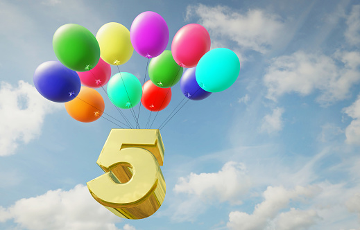 Golden number five flies high in the sky in balloons. Happy birthday and anniversary