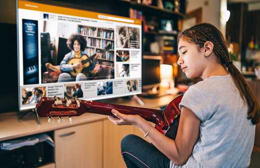 Girl playing a guitar with video online teleconferencing at home in isolation