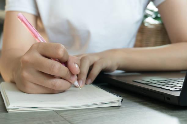 istock Young business woman sitting at table with laptop and taking notes in notebook. 1217545748