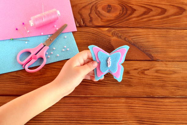 istock A small child holds a felt butterfly crafts in his hand. Sewing kit to make projects. Brown wooden table. Hand sewing projects for kids teaching 1217546516