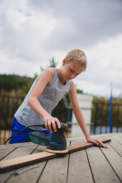 istock Boy sanding a wooden plank down with an electrical orbit sander 1217546538