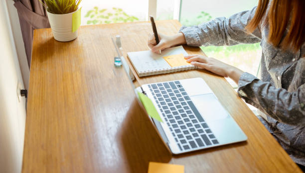 istock Close up woman working from home writing project, Prevent the spread of coronavirus quarantine for covid-19 work desk with laptop computer and protectiv, Self isolation from society to reduce risks. 1217547730
