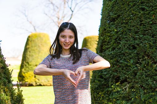 Young beautiful Chinese woman is showing heart shape gesture in a park
