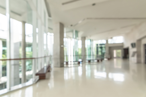 Hotel or office building lobby blur background interior view toward reception hall, modern luxury white room space with blurry corridor and building glass wall window