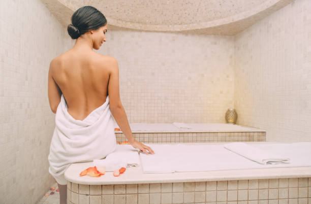 Beautiful mixed race woman with open back sitting on a marble massage table in a hammam. Body recovery at hamam, turkish bath Beautiful mixed race woman with open back sitting on a marble massage table in a hammam. Body recovery at hamam, turkish bath turkish culture photos stock pictures, royalty-free photos & images