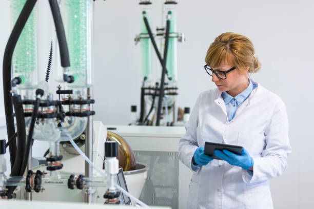 istock Scientist with tablet operating rotational vaporizer with green condenser. She is wearing latex gloves and glasses. CBD hemp oil extraction is in rotational flask. 1217557913