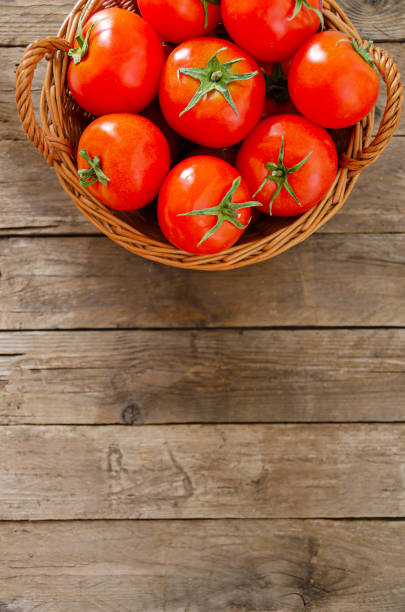 istock Wicker basket with tomatoes on an old wooden table. 1217557915
