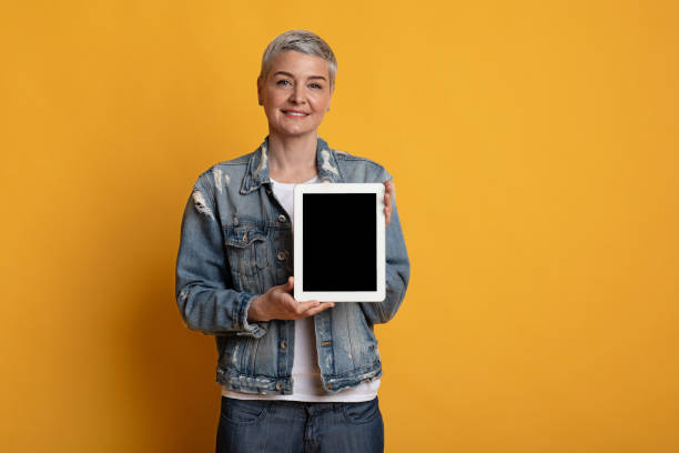 istock Beautiful middle aged woman showing digital tablet with blank black screen 1217557987