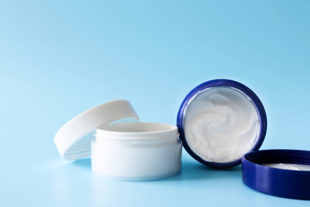 istock Opened moisturizer cream in white plastic jars on blue background, front view. Mockup cosmetic branding 1217558477