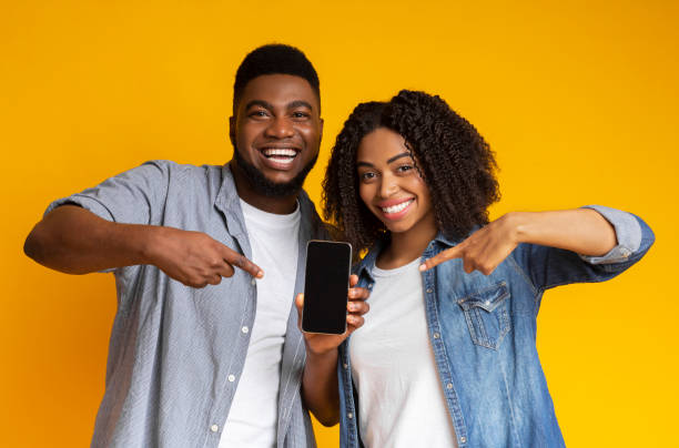 istock Cheerful african couple pointing at smartphone with black screen for mockup 1217558682