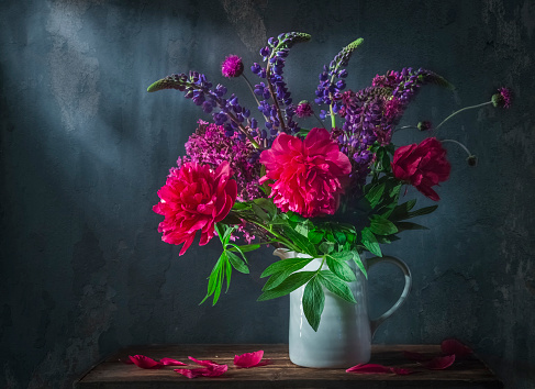 Classic still life with beautiful purple peony and lupin flowers bouquet in white jug. Art photography.