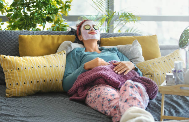 Enjoying my little spa time at home. Young woman in pajamas, with face mask and slices of cucumber over her eyes, lying on the bed. She's enjoying every minute of it. relaxation lying on back women enjoyment stock pictures, royalty-free photos & images